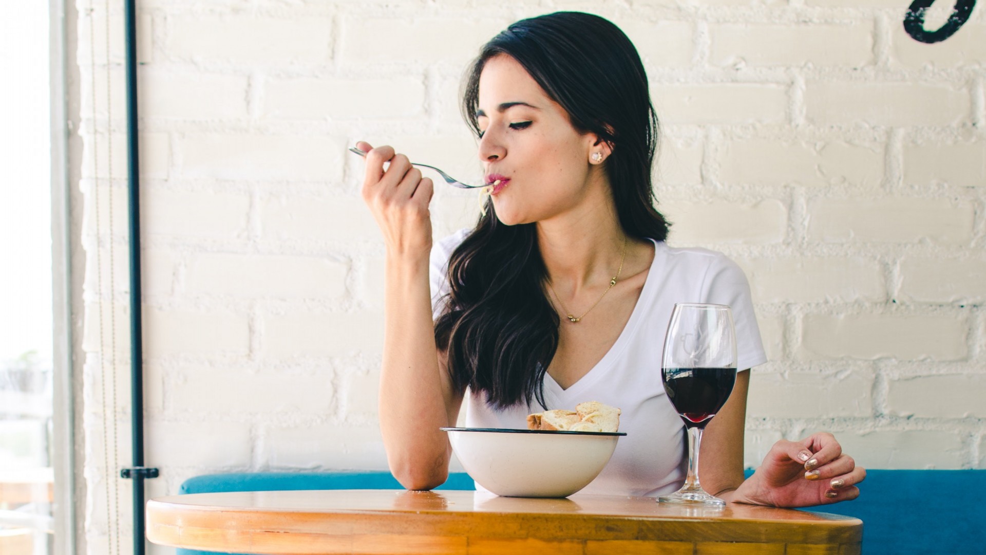 Woman eating a pasta with relish and drinking a glass of red wine